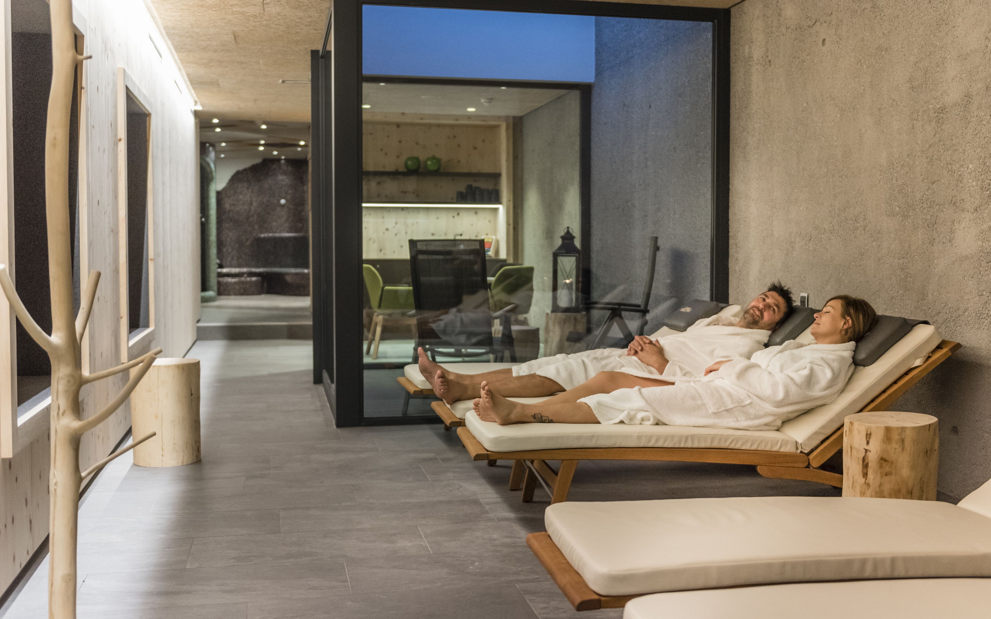 Ein Spa-Raum mit zwei Liegestühlen, Holzboden und einer Glastür zu einem Essbereich.
