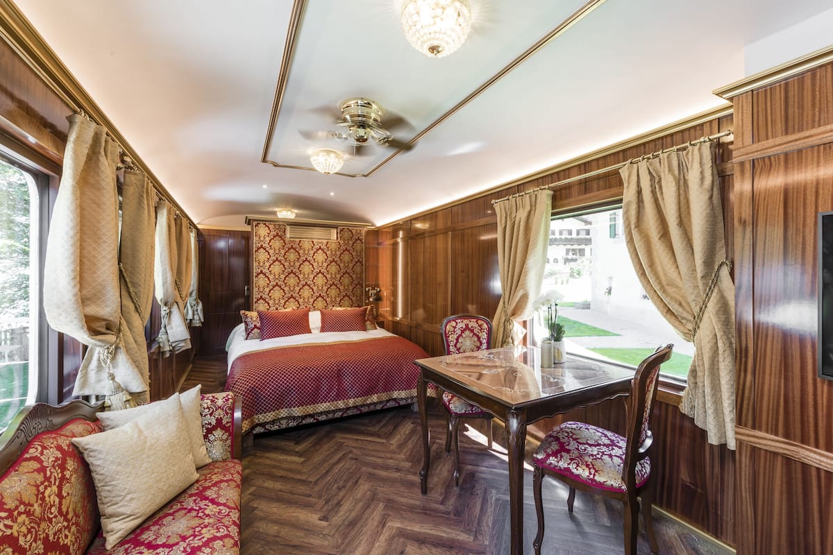 A room with a bed, a table, and a chair, with curtains and a window.