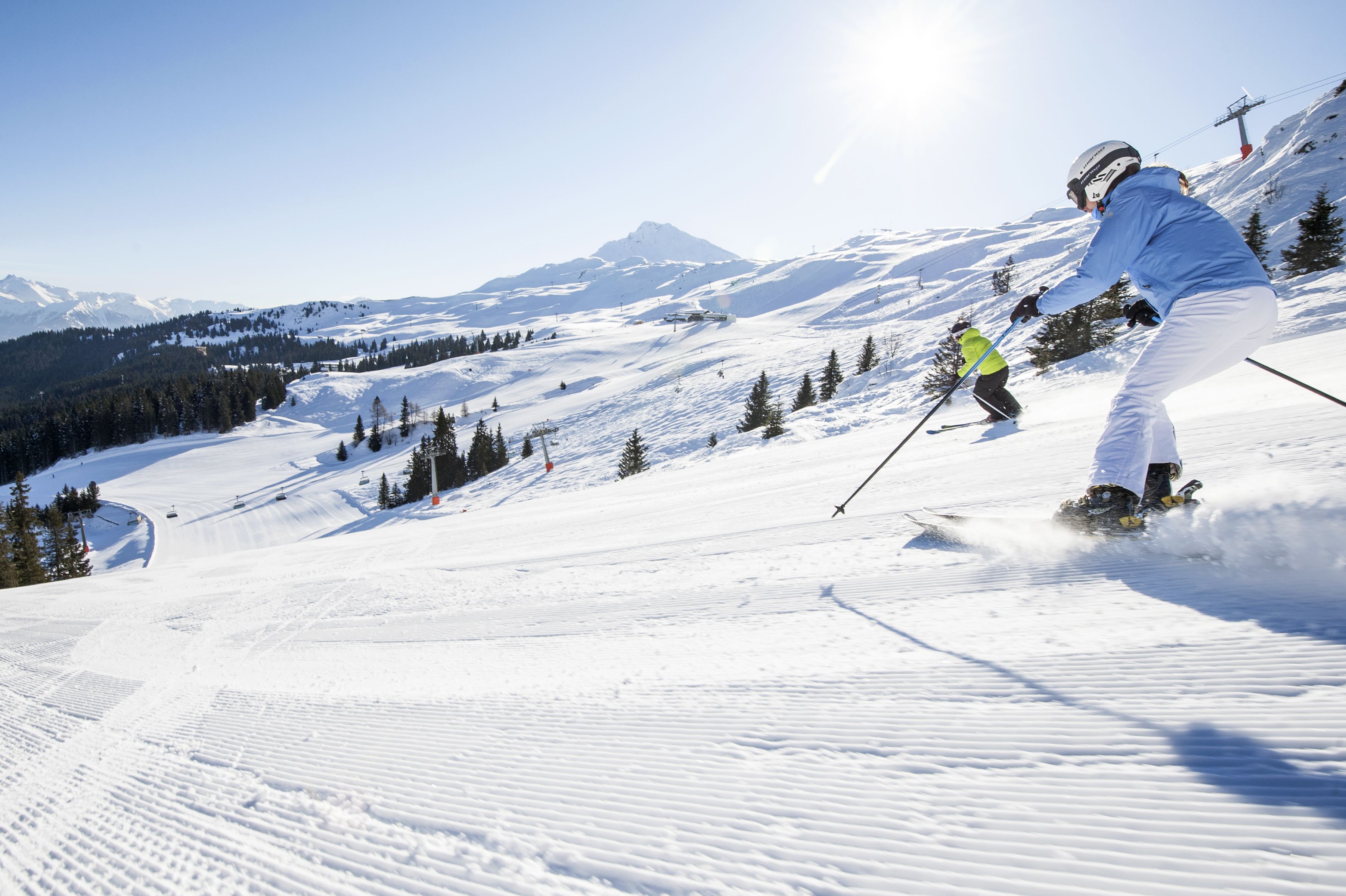 A snowy ski slope with skiers, a clear sky, and a mountain in the background.