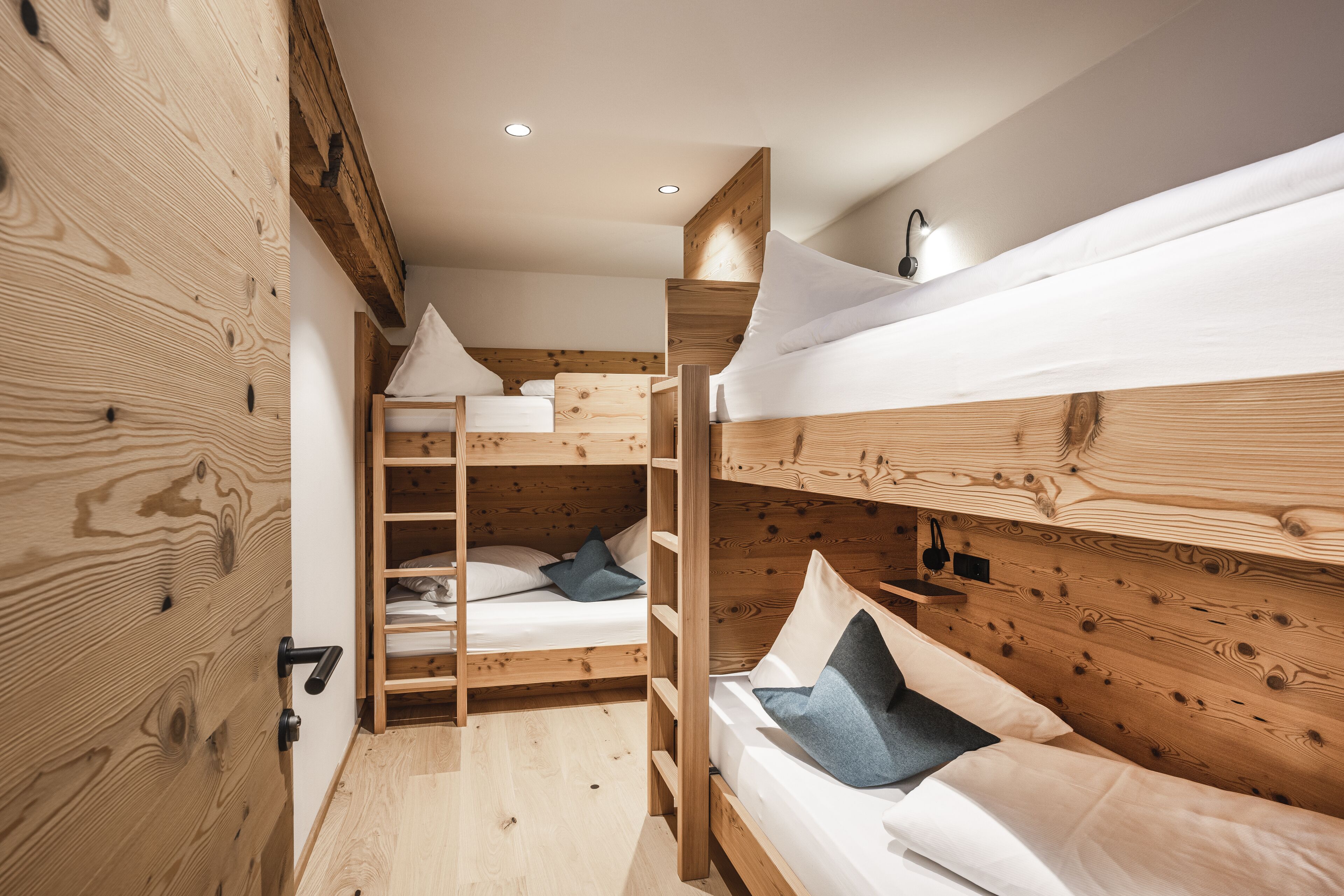 A wooden bunk bed room with a ladder, white bedding, and a small shelf with a light.