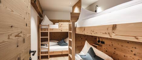 A wooden bunk bed room with a ladder, white bedding, and a small shelf with a light.