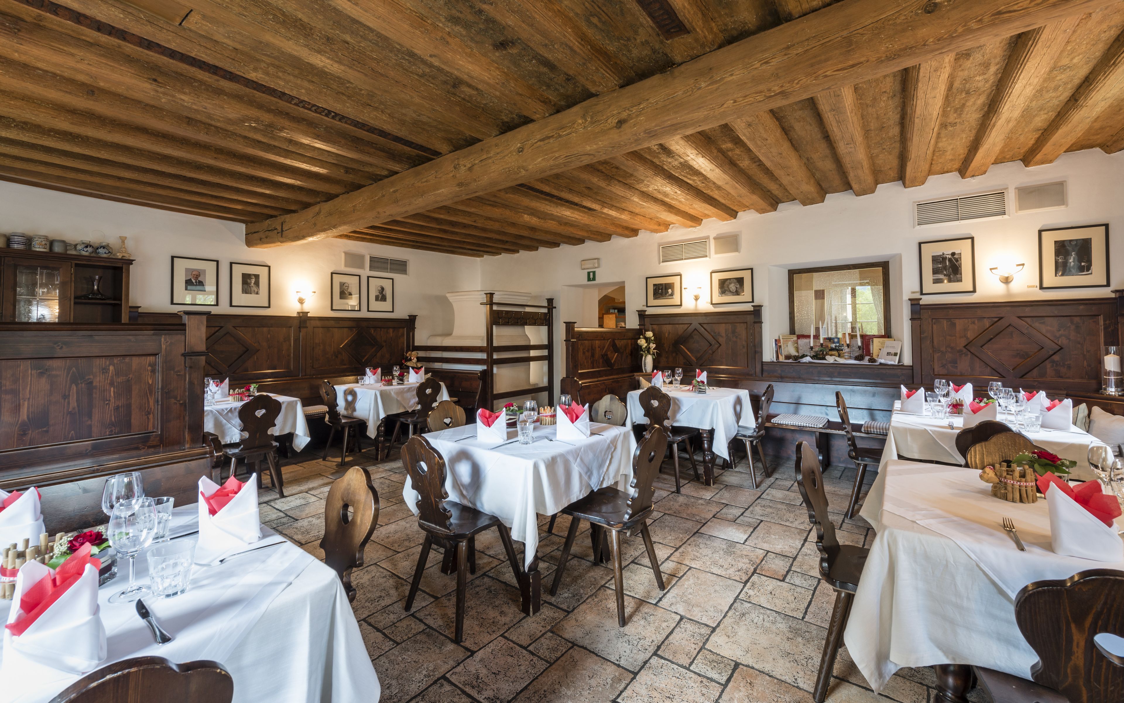 A restaurant with wooden beams, white tablecloths, and framed pictures on the walls.