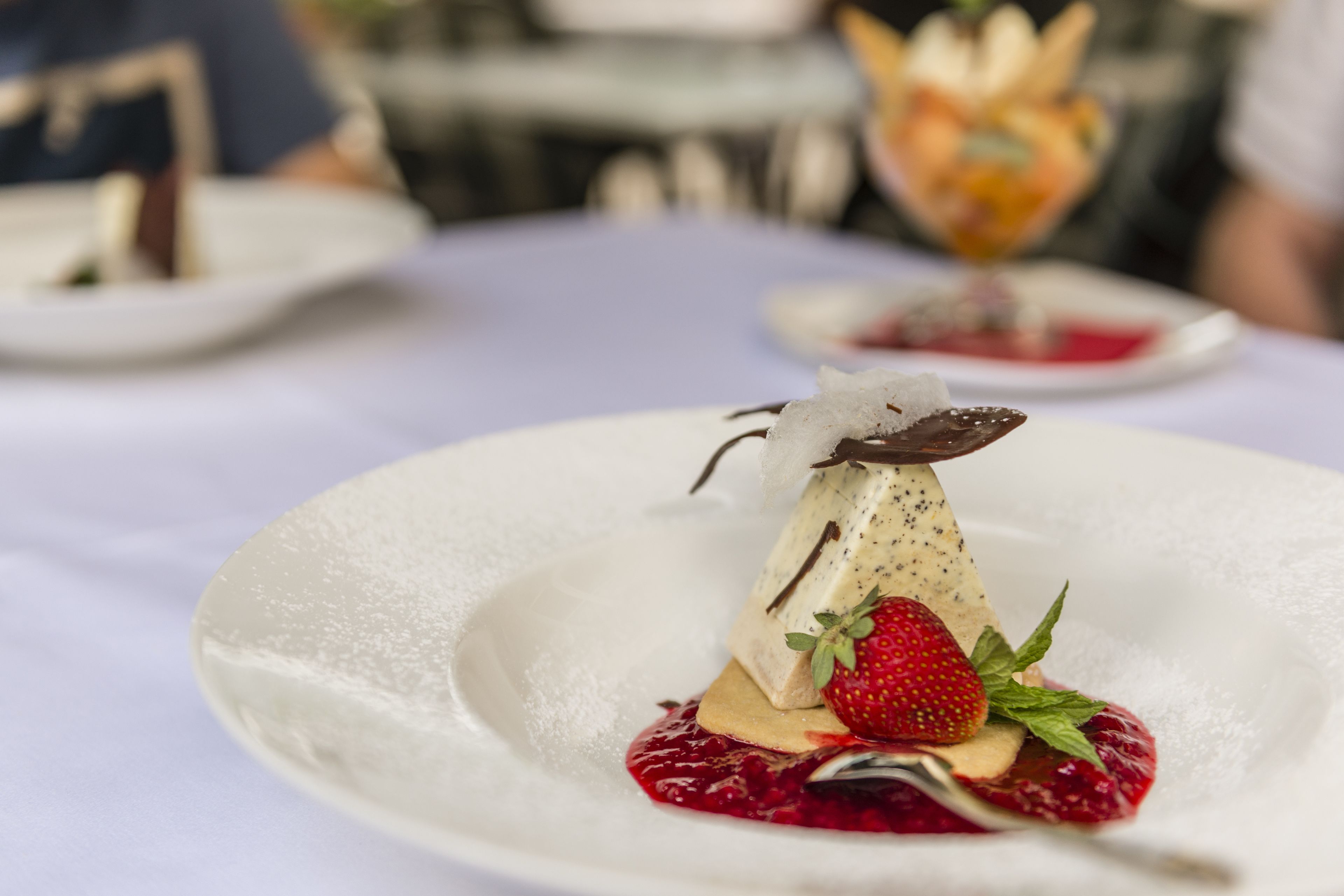 Un dessert servi dans une assiette blanche, décoré d’une fraise et de quelques feuilles de menthe.