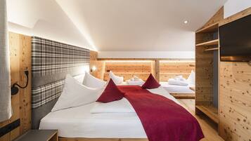 Ein modernes Hotelzimmer mit einem hölzernen Kopfteil, einem großen Bett mit weißen Bettwäsche und roten Kissen, einem Holzschrank und einem Flachbildfernseher.
