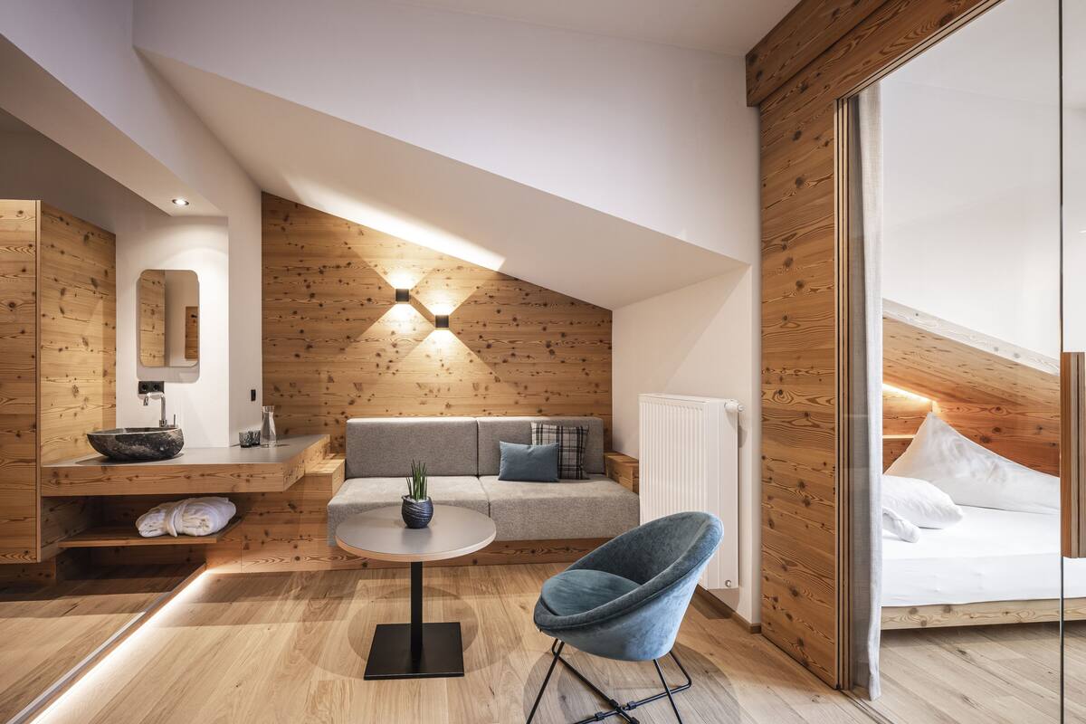 A modern loft bedroom with a wooden ceiling, a round table, a blue chair, a sofa, and a bed.