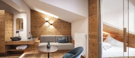 A modern loft bedroom with a wooden ceiling, a round table, a blue chair, a sofa, and a bed.