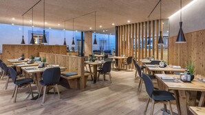 A modern restaurant with wooden furniture and a high ceiling. Tables are arranged for dining, and there are large windows providing views of the outside. - Lener Wirtshaus & Hotel (Campo di Trens)