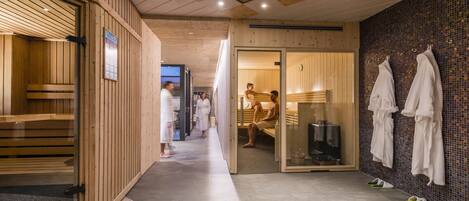 Un área de spa con bancos de madera, una pared con azulejos y una puerta de cristal que da a una habitación.