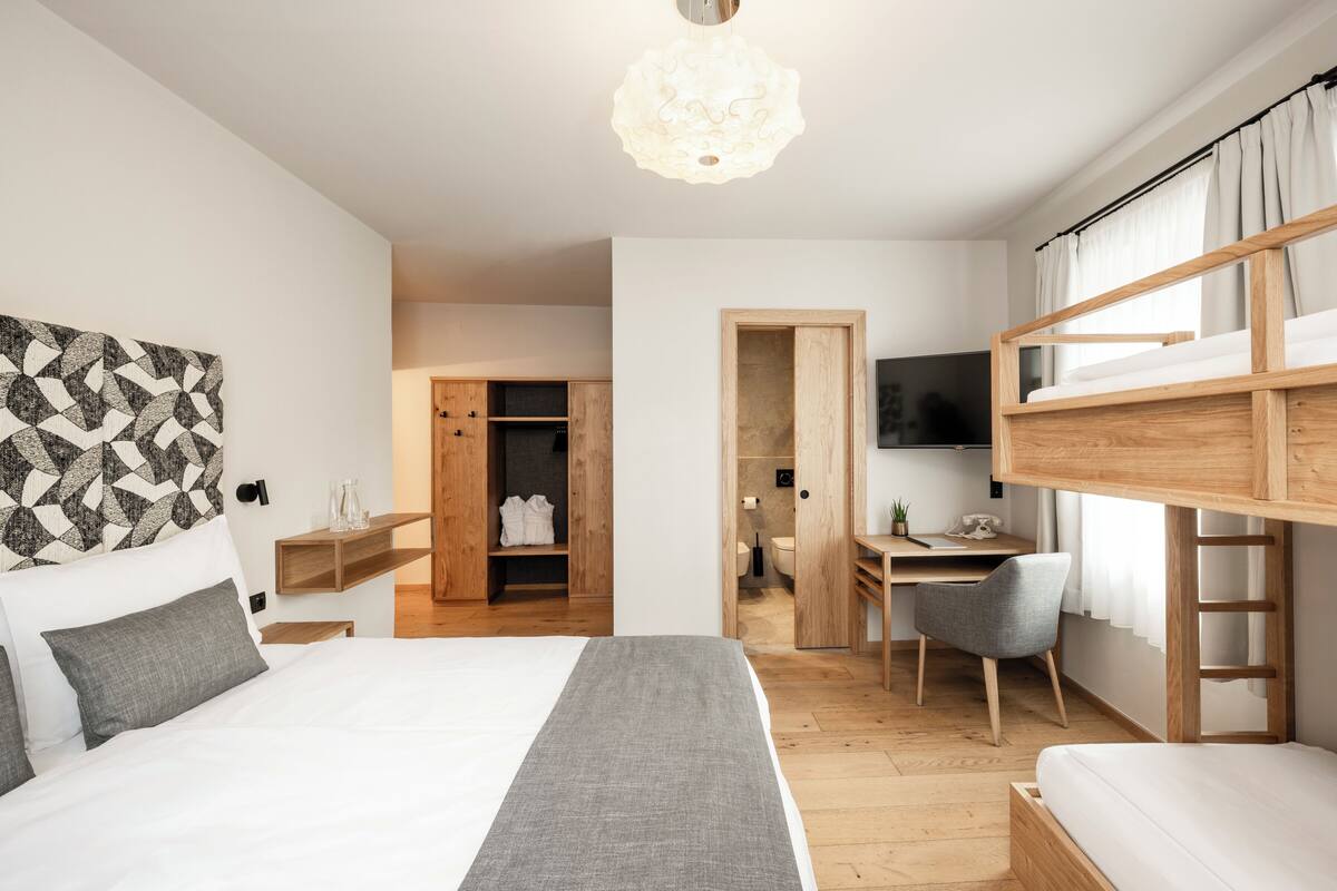 A modern bedroom with a bunk bed, a desk with a chair, a television, and a wardrobe.