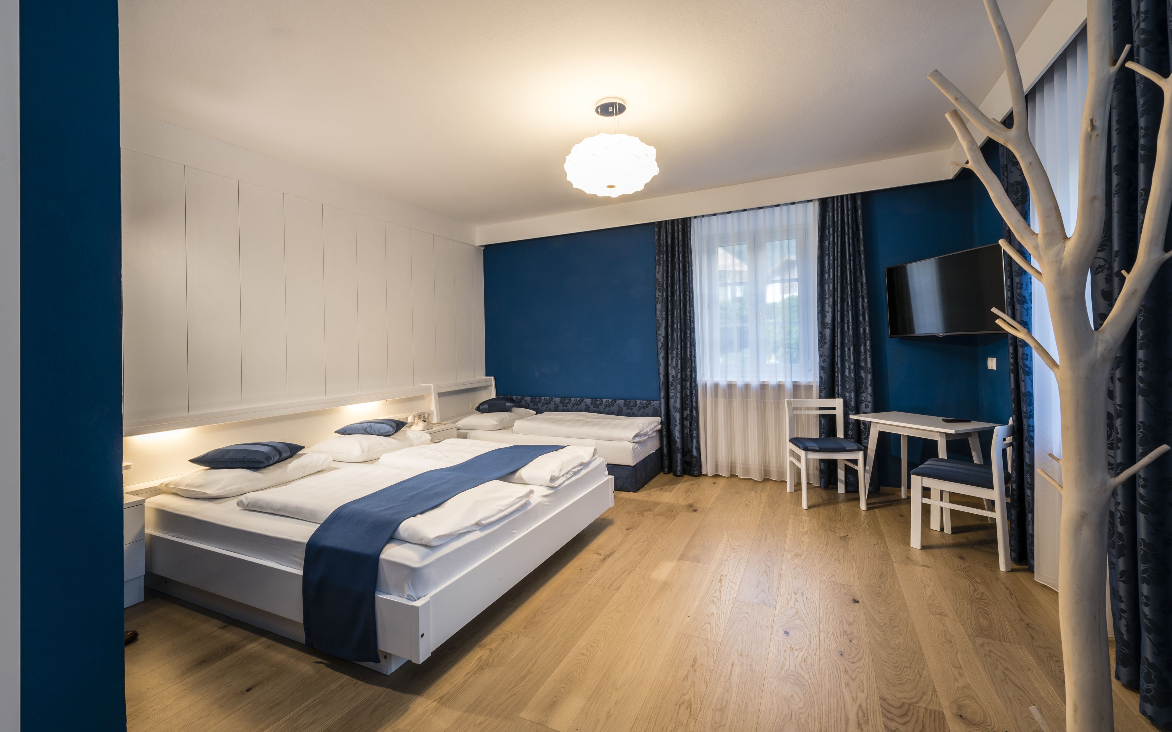 Habitación de hotel con dos camas, un escritorio, una silla, un televisor y un adorno decorativo con forma de árbol.