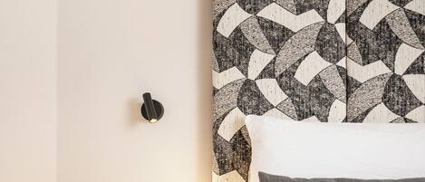 A neatly made bed with a patterned headboard, a bedside table with a telephone, and a wall-mounted light fixture.