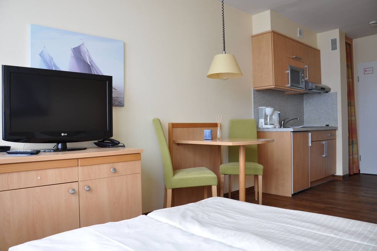 Une chambre d’hôtel comprenant un lit, une télévision, un bureau avec une chaise, une kitchenette et un tableau au mur.