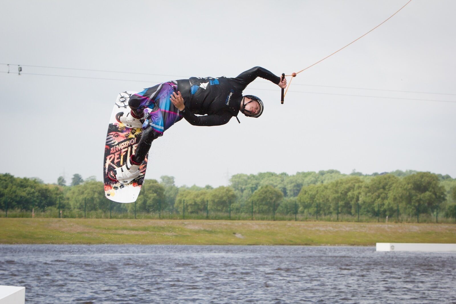 Uma pessoa praticando kitesurf sobre a água, com árvores ao fundo.