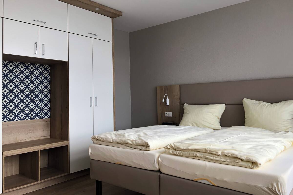 Une chambre à coucher comprenant un lit, une armoire, une table de chevet et une lampe fixée au mur.