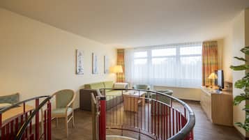 A spacious living area with a staircase, a sofa, a coffee table, and a TV on a wooden cabinet.