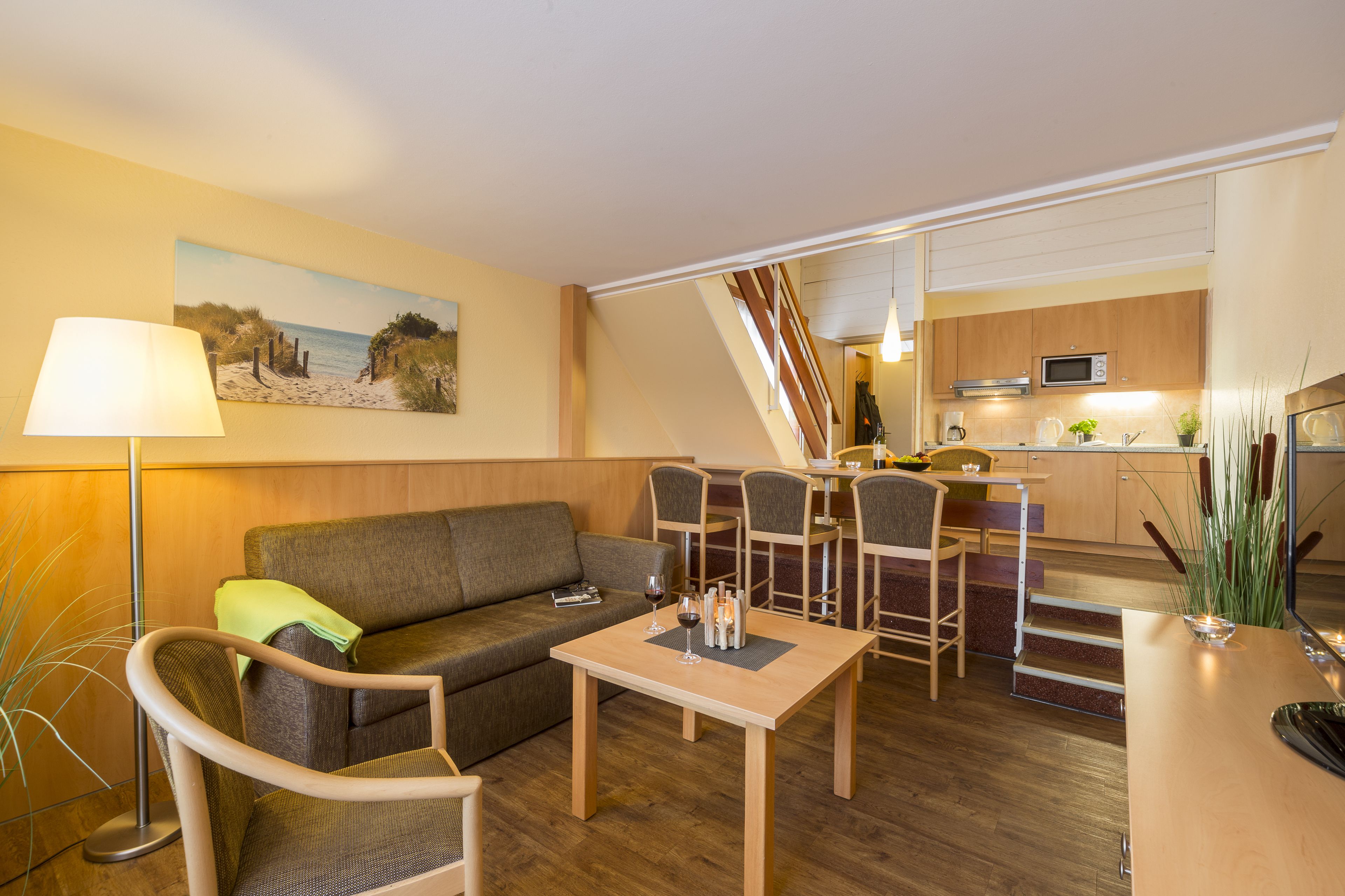 Ein kompakter Wohnbereich mit Sofa, Esstisch, Stühlen, einer Küchenzeile und einer Treppe zu einer oberen Ebene.