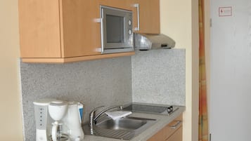 Een compacte keuken met houten kastjes, een magnetron, een koffiezetapparaat en een spoelbak.