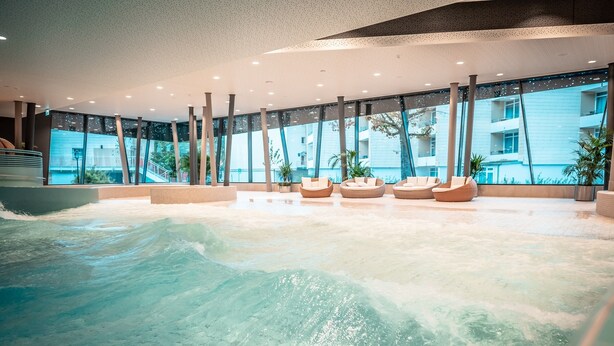 Una piscina interior moderna con agua cristalina, ventanas amplias y zonas de estar.