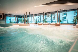 Una piscina interior moderna con agua cristalina, ventanas amplias y zonas de estar.