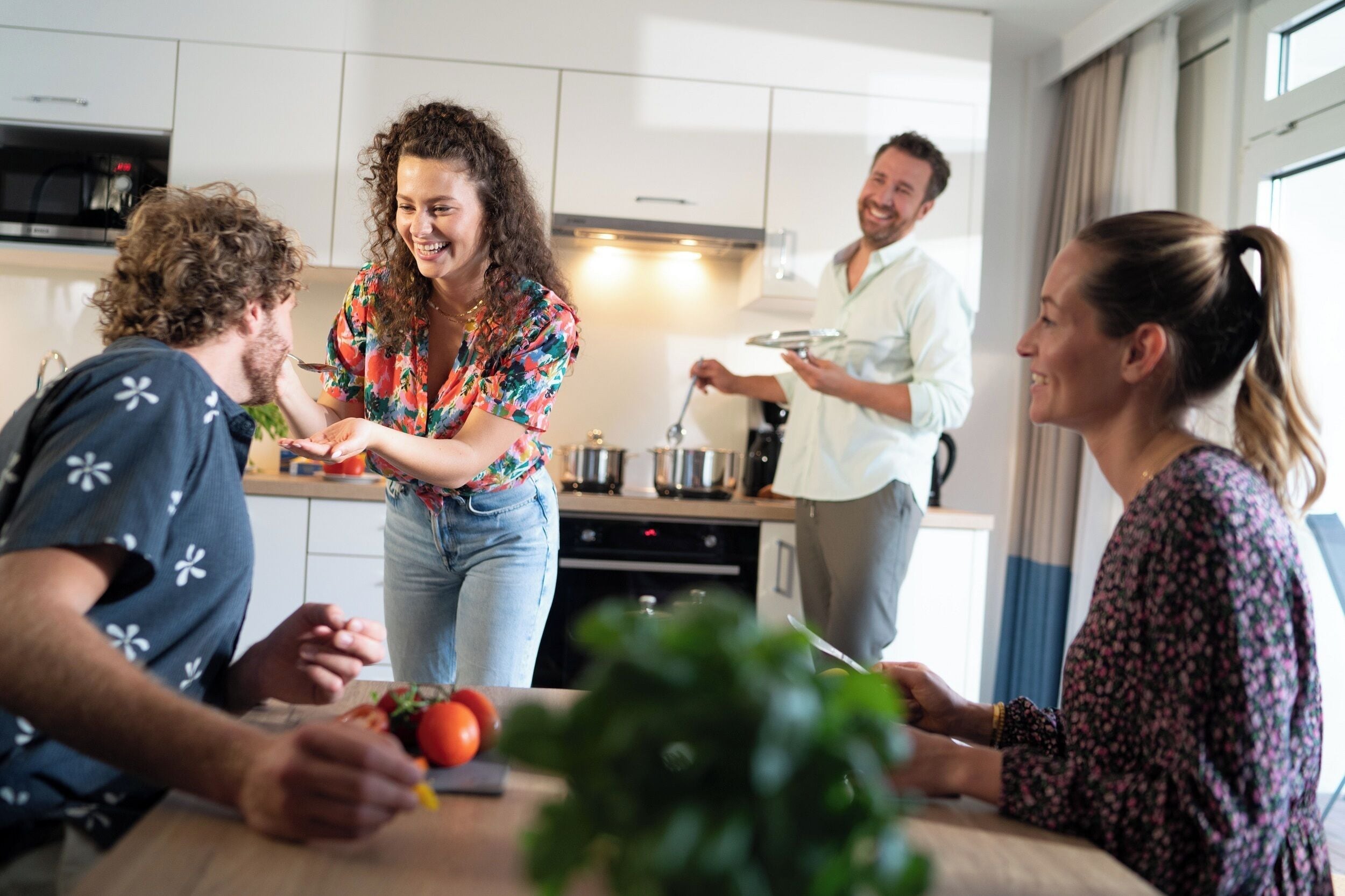 Een moderne keuken met witte kasten, een eettafel waar mensen aan het eten zijn, en een raam met gordijnen.
