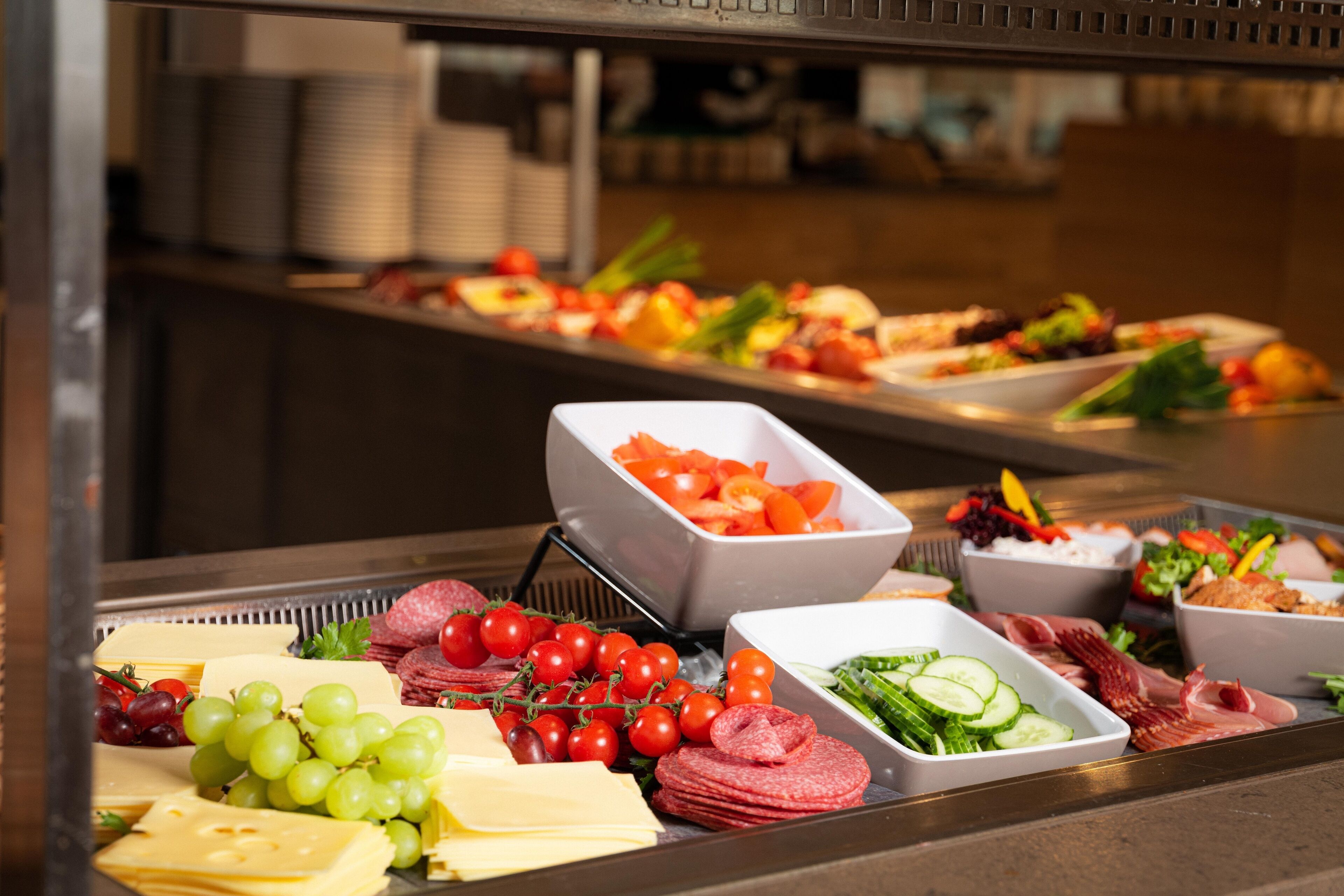 Un buffet proposant une variété d’aliments, notamment du fromage, des raisins, des tomates et de la charcuterie.