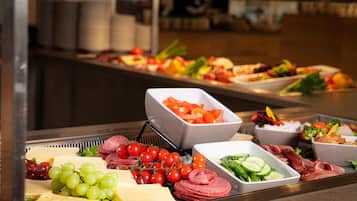 Un buffet proposant une variété d’aliments, notamment du fromage, des raisins, des tomates et de la charcuterie.
