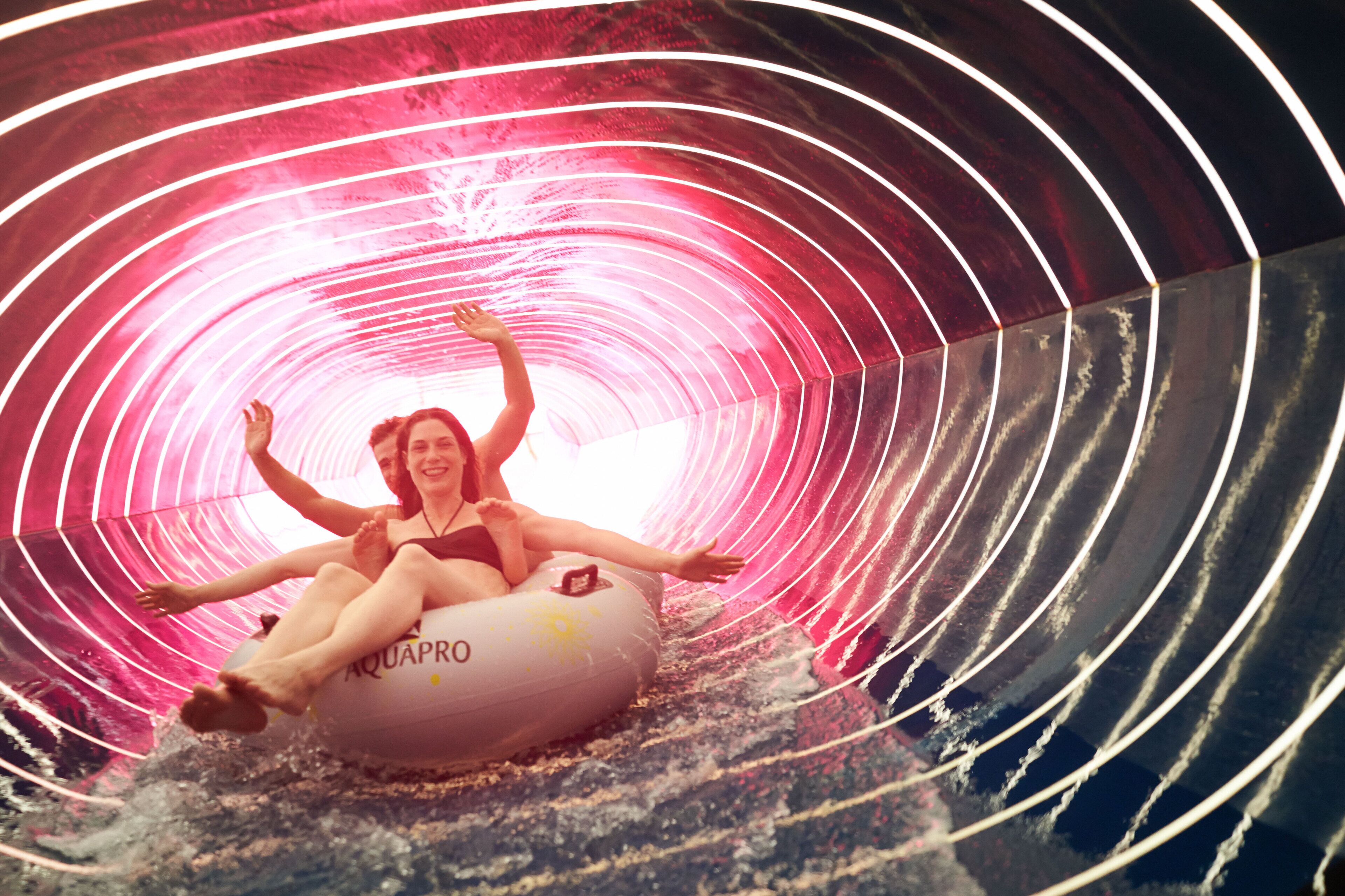 A person on an inflatable tube in a tunnel with a pink and white striped pattern.