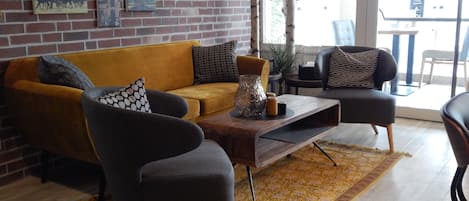 A modern living room with a brick wall, a yellow sofa, two armchairs, a coffee table, and a patterned rug.