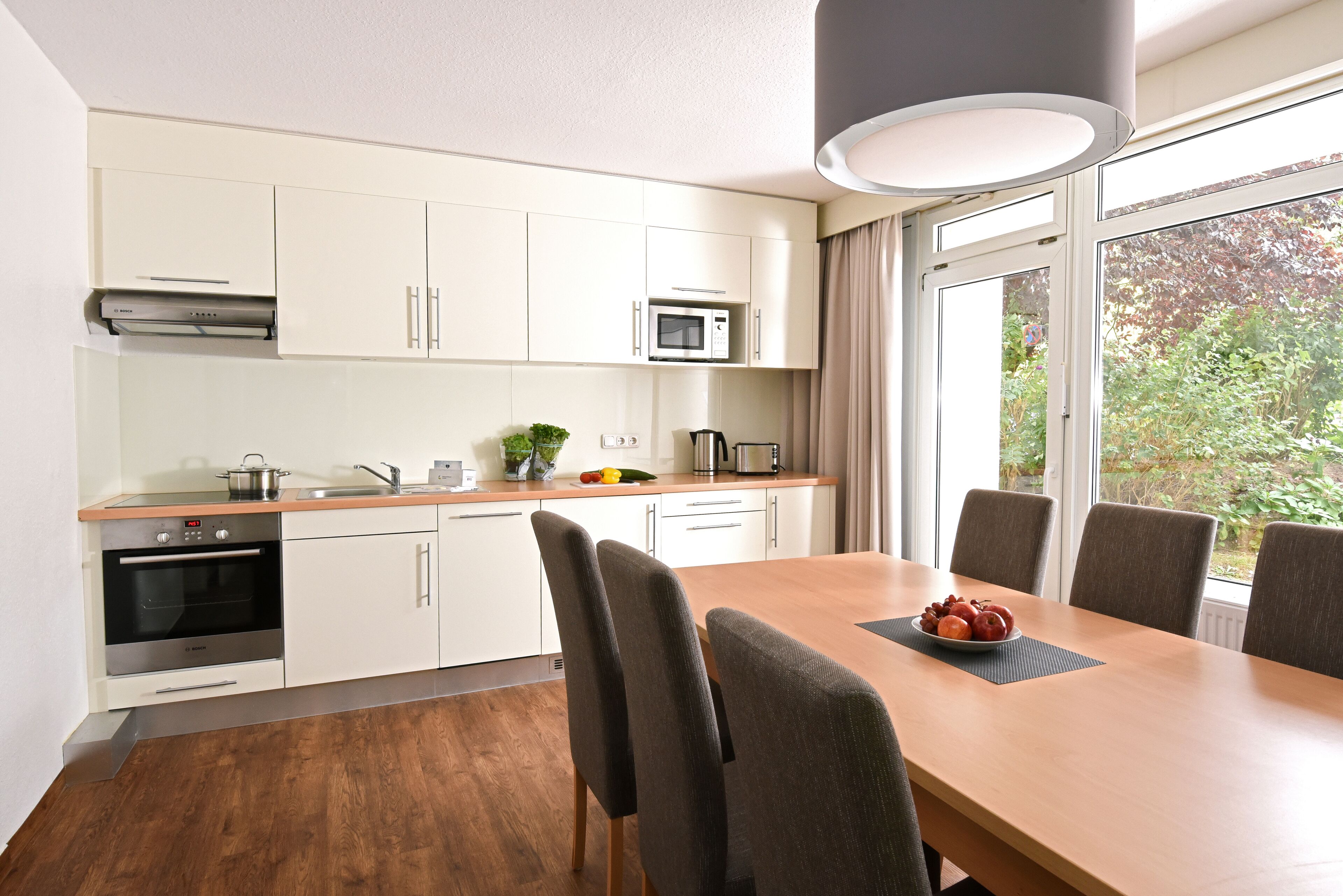 Une cuisine moderne avec des meubles blancs, un four à micro-ondes et un coin repas comprenant une table et des chaises en bois.