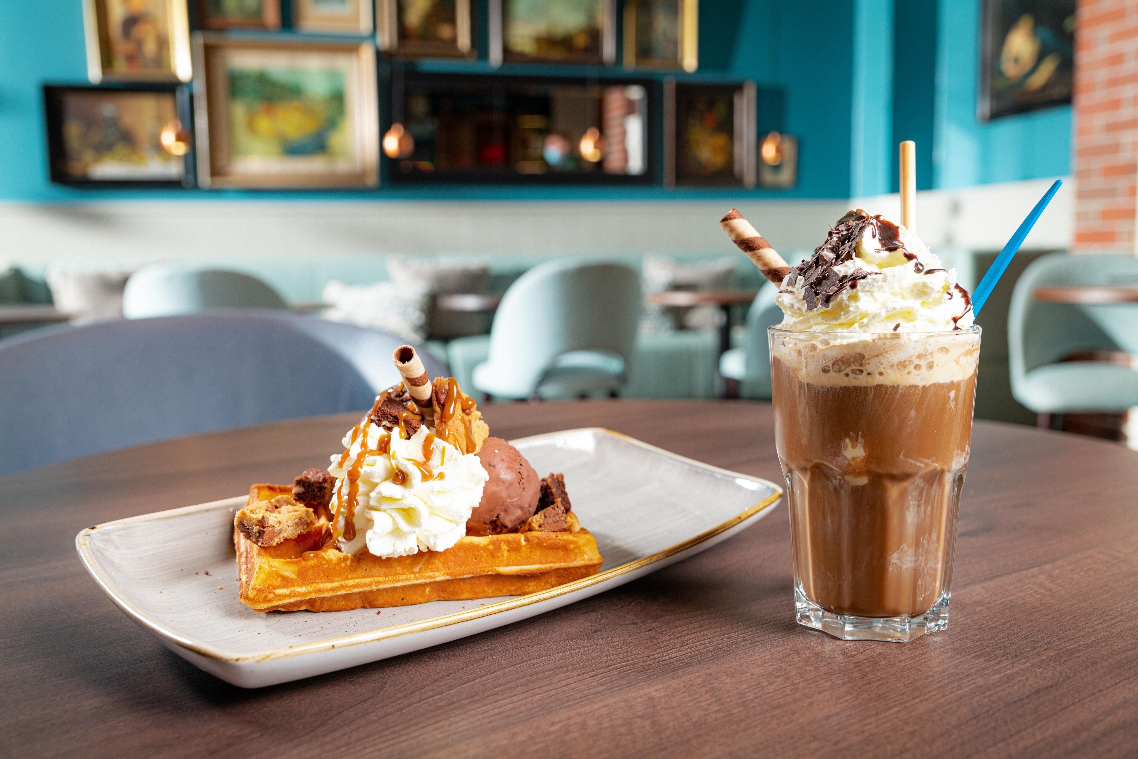 Une assiette de dessert avec une gaufre et une boule de glace, ainsi qu’un verre de café glacé, sur une table dans un restaurant.