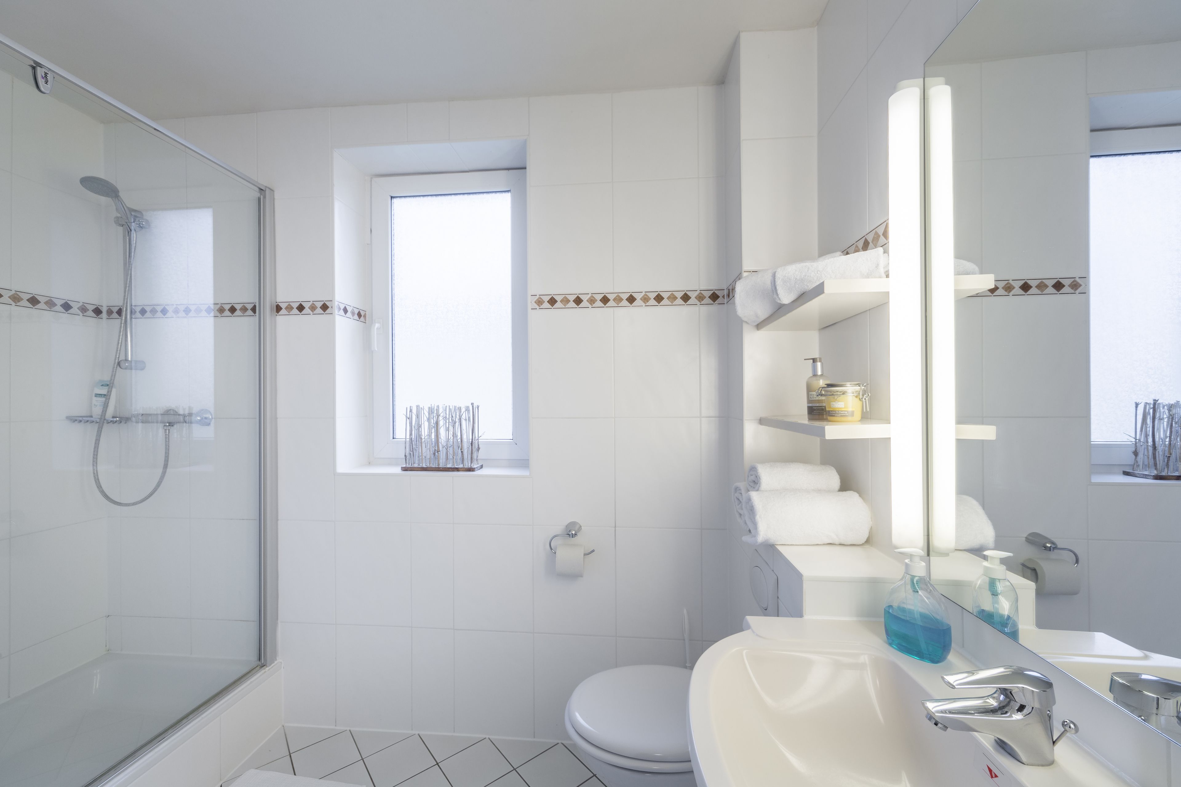 A modern bathroom with a glass shower enclosure, a toilet, a sink with a mirror, and a window.