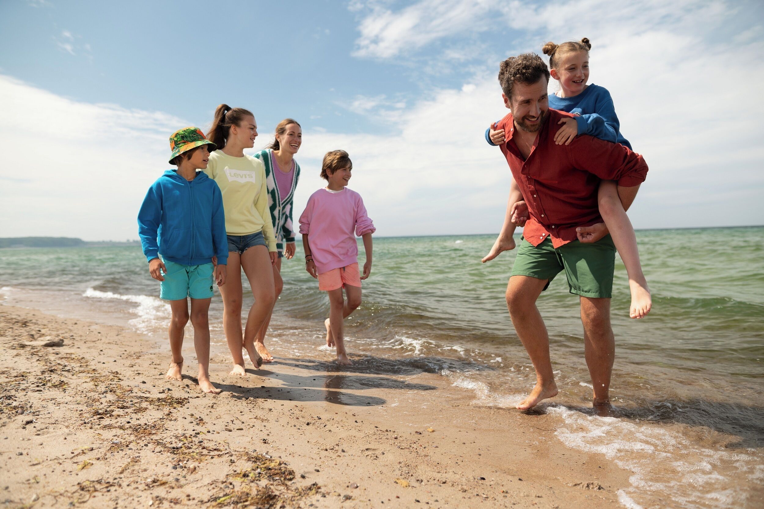 Un grupo de personas caminando sobre una playa arenosa con el océano al fondo.