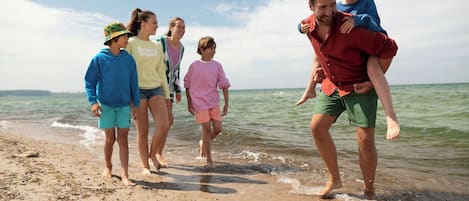 A group of people walking along a sandy beach with the ocean in the background.