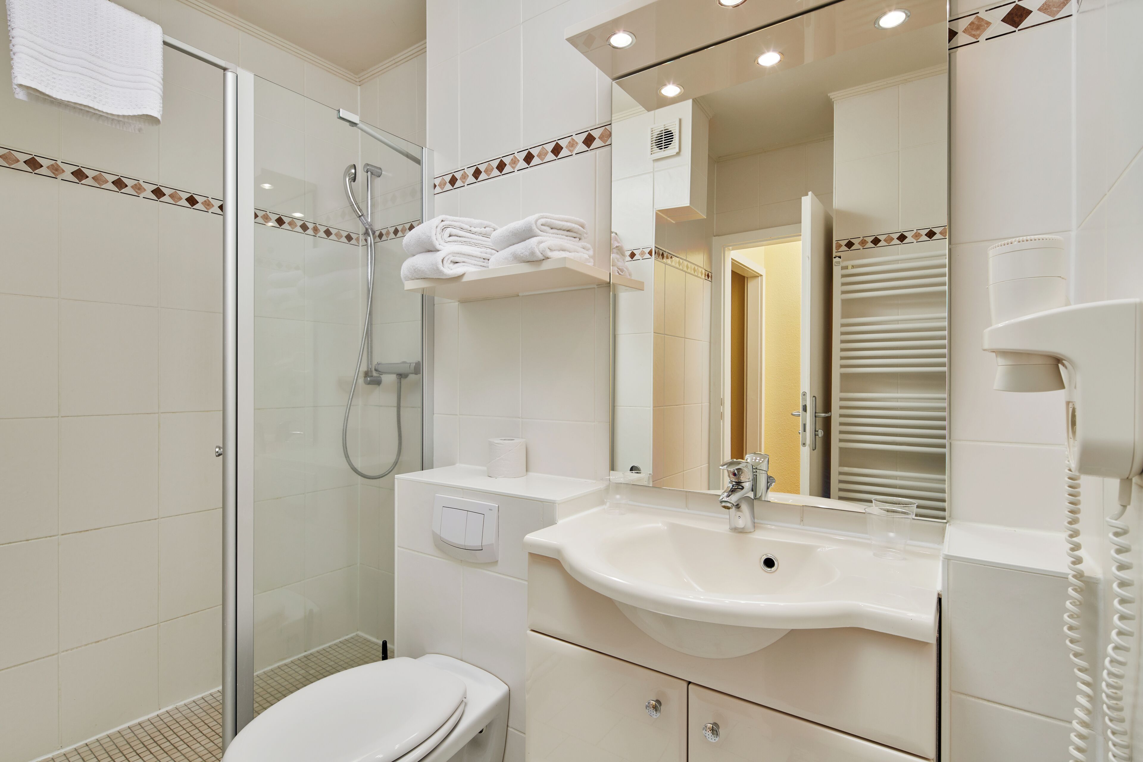 Un baño con cabina de ducha de vidrio, un lavabo blanco, un inodoro y un espejo con toallero.