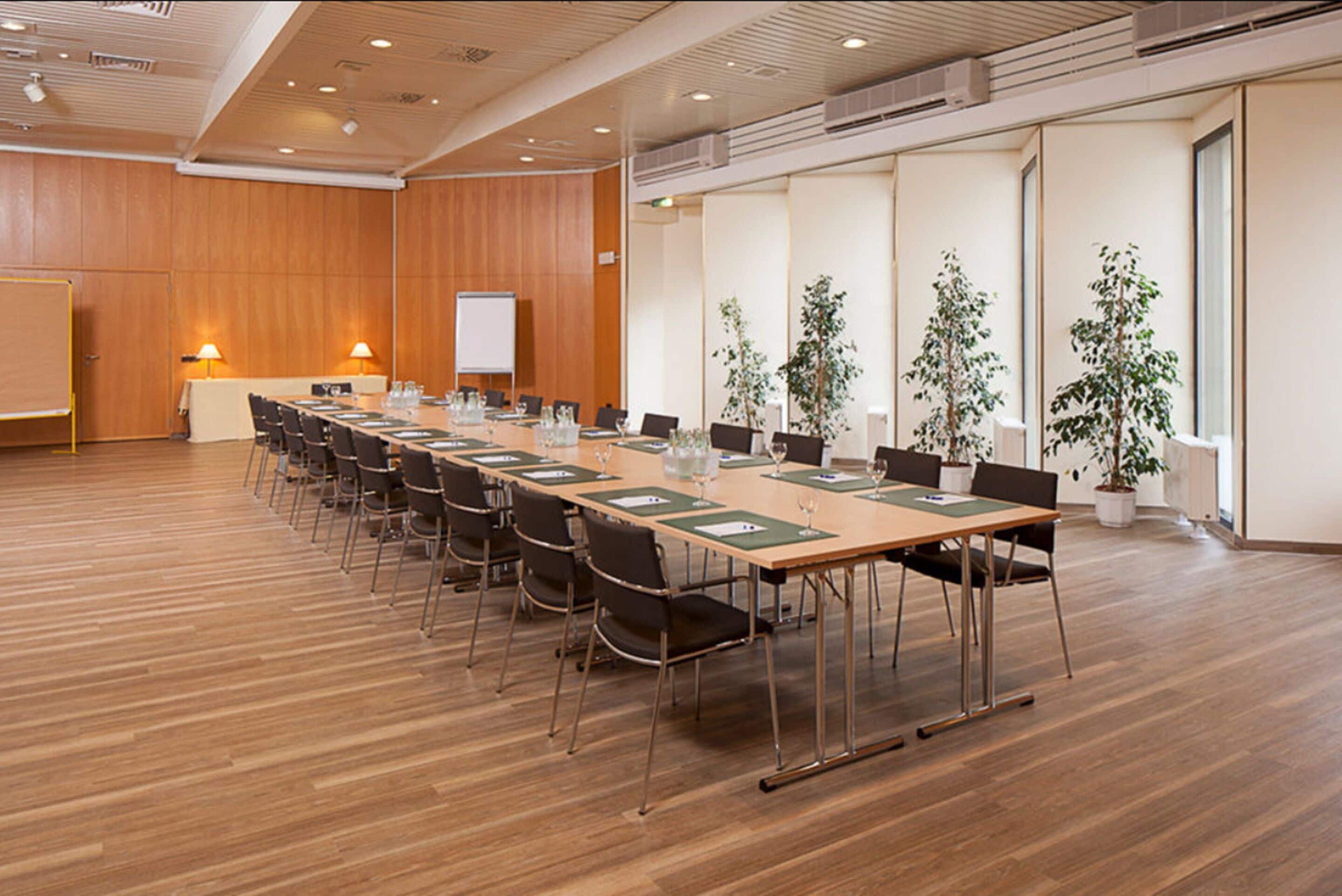 Une salle de conférence avec une longue table, des chaises, un tableau blanc et des plantes en pot.