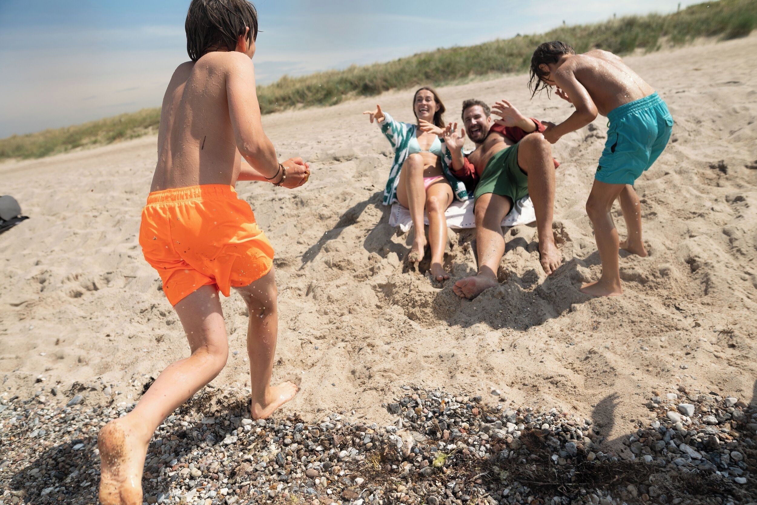 A group of people on a sandy beach with some sitting and others standing, engaging in beach activities.