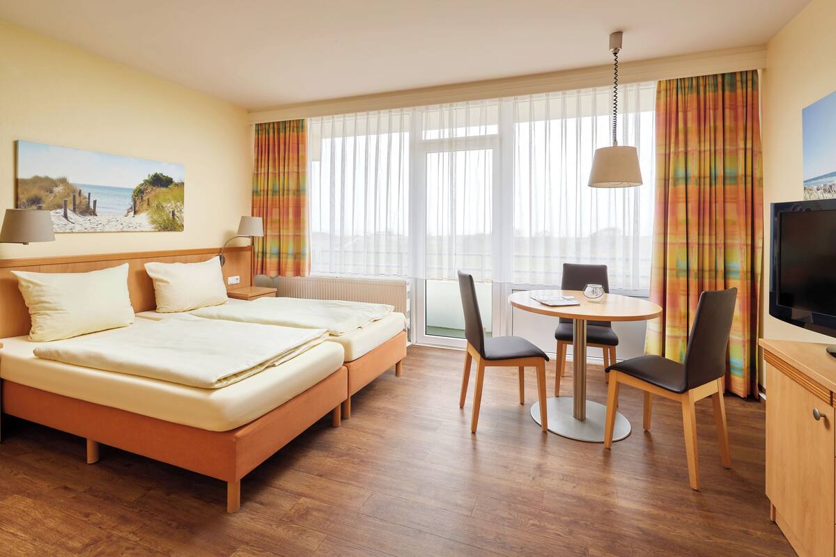 Une chambre d’hôtel avec un lit, un bureau, une chaise, une télévision et une fenêtre avec des rideaux.