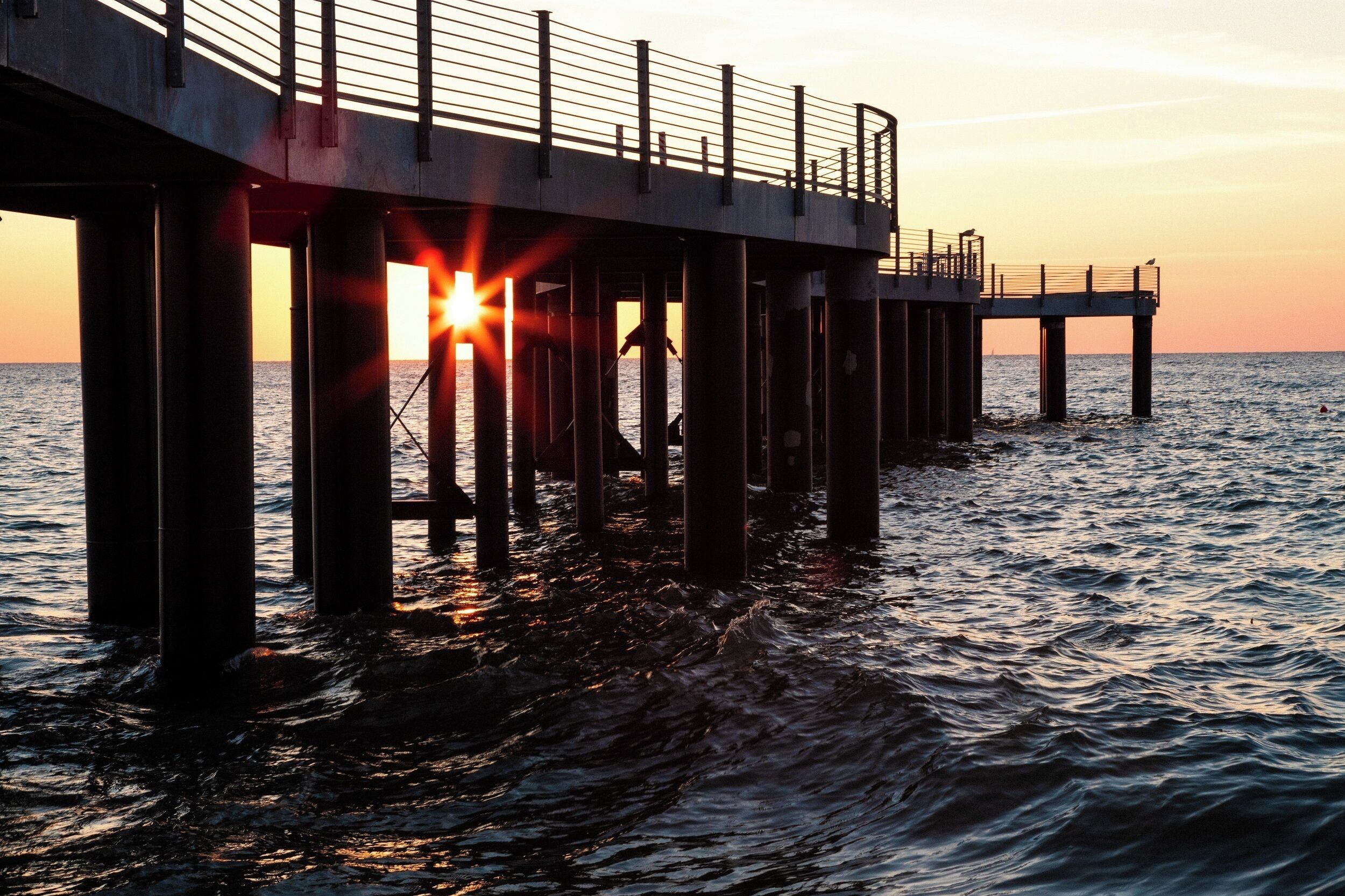 A pier extending into the water with a sunset in the background.
