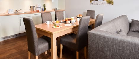 Una cucina moderna con mobili bianchi, un tavolo da pranzo in legno e un divano grigio.