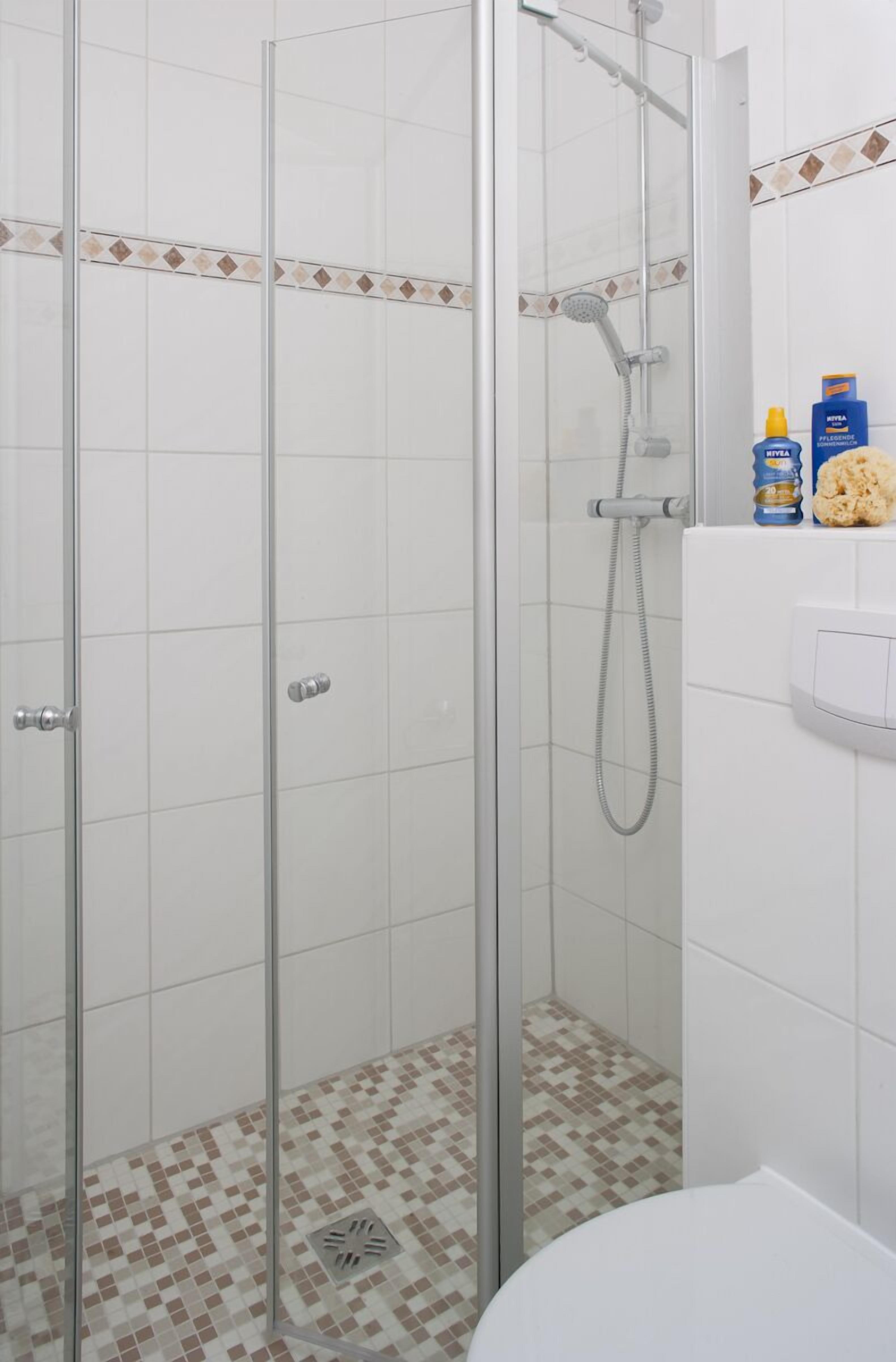 Cabina de dutxa amb vidre, sòl de rajoles, vàter i vàter de mà.