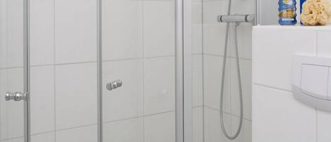 Cabina de dutxa amb vidre, sòl de rajoles, vàter i vàter de mà.