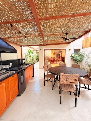A modern kitchen with a black stove, wooden cabinets, and a dining area with a round table and wicker chairs. - Pousada Pantai Maresias (São Sebastião)