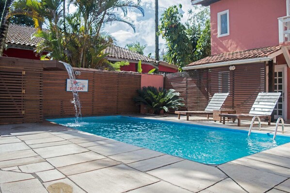A swimming pool with a wooden fence, lounge chairs, and a sign that reads "Pool Area". - Pousada Pantai Maresias (São Sebastião)