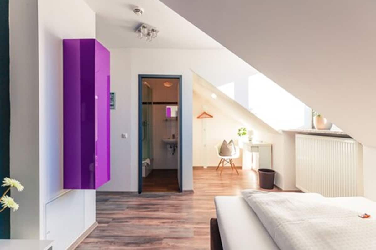 A modern bedroom with a sloped ceiling, a bed, a small table, and a chair.