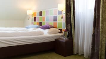 A hotel room with a bed, pillows, a nightstand, a lamp, and curtains.
