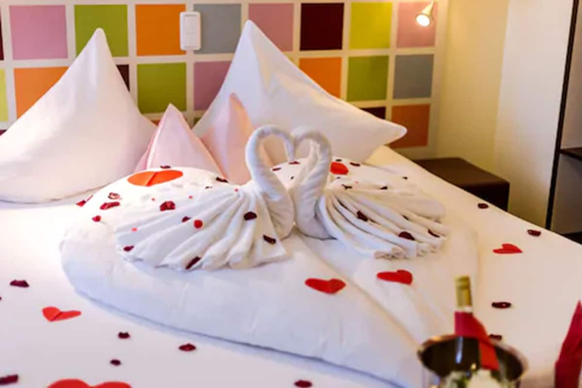 A bed with a white bedspread, two white pillows, and a decorative swan made of towels.