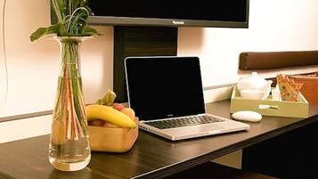 Un ordinateur portable est posé sur un bureau, à côté d’un vase de fleurs, d’un panier de fruits et d’une théière.