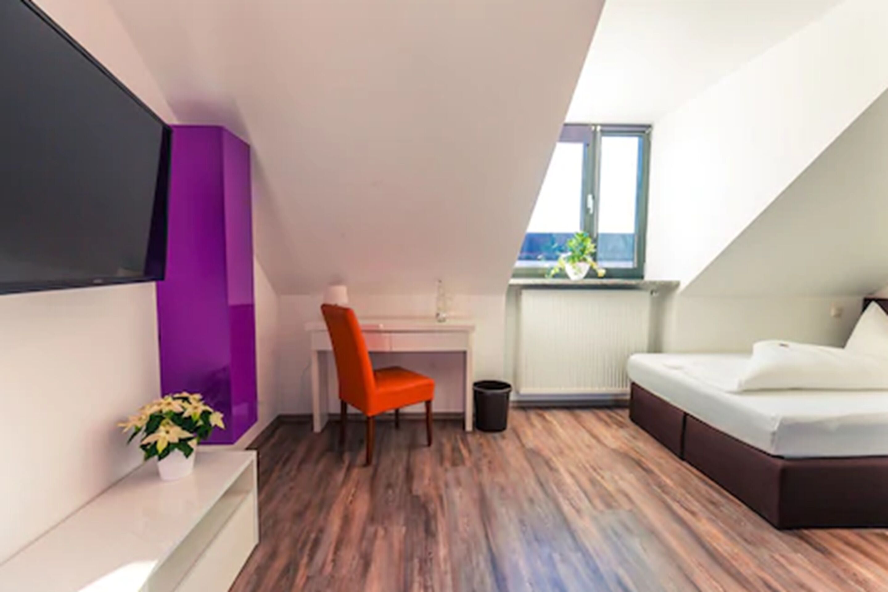Une chambre moderne avec un plafond en pente, un bureau, une chaise, un lit et une fenêtre donnant sur un beau paysage.