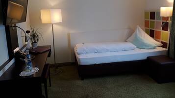 Habitación de hotel con cama, escritorio con lámpara, televisor y un panel de pared colorido.