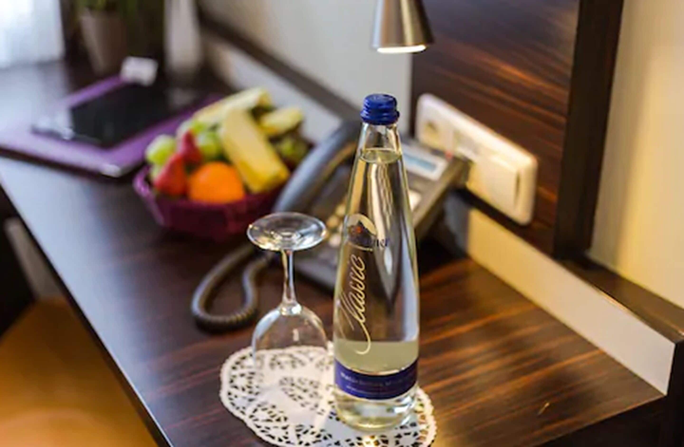 A bottle of water, a glass, and a fruit bowl on a wooden table.